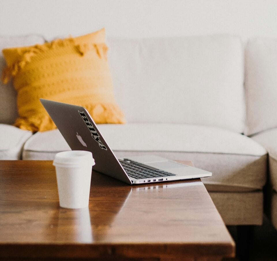 Omenasiivous Kannettava tietokone ja kahvikuppi siistillä sohvapöydällä. Kuva symboloi helppoa yhteydenottoa siivouspalveluun liittyen.