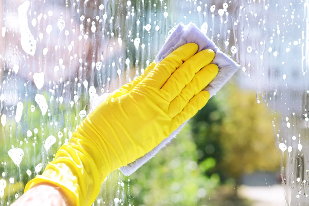 Ikkunanpesu: Lähikuva, jossa siivooja pesee ikkunaa huolellisesti.